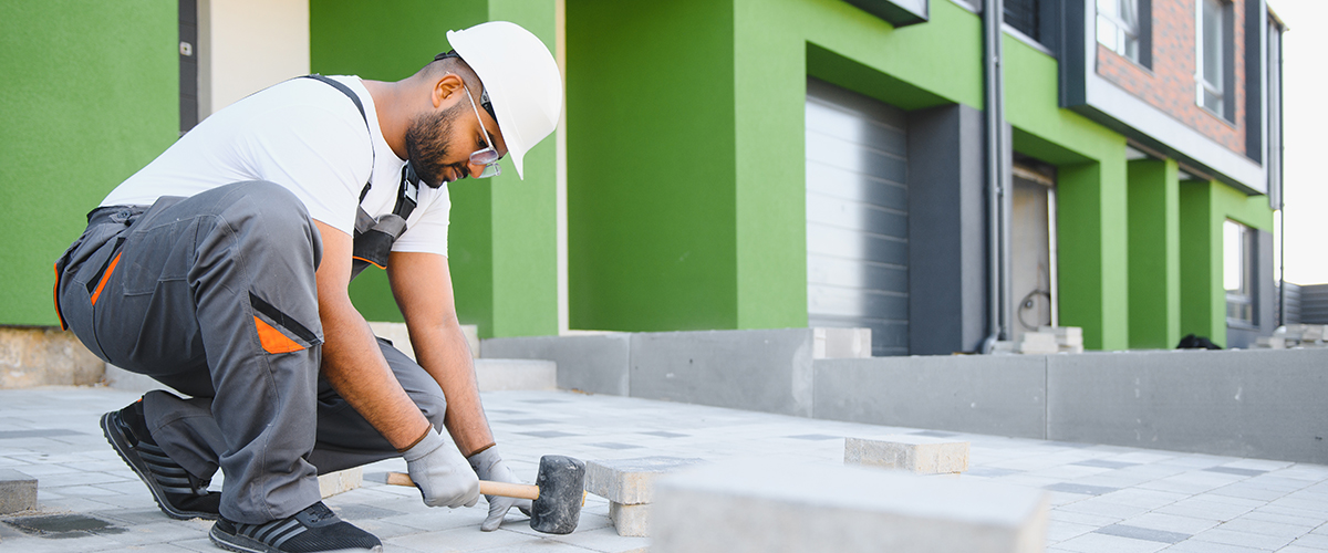 Mitarbeiter führt Pflasterarbeiten rund ums Haus aus und erstellt saubere, stabile Wege und Flächen.